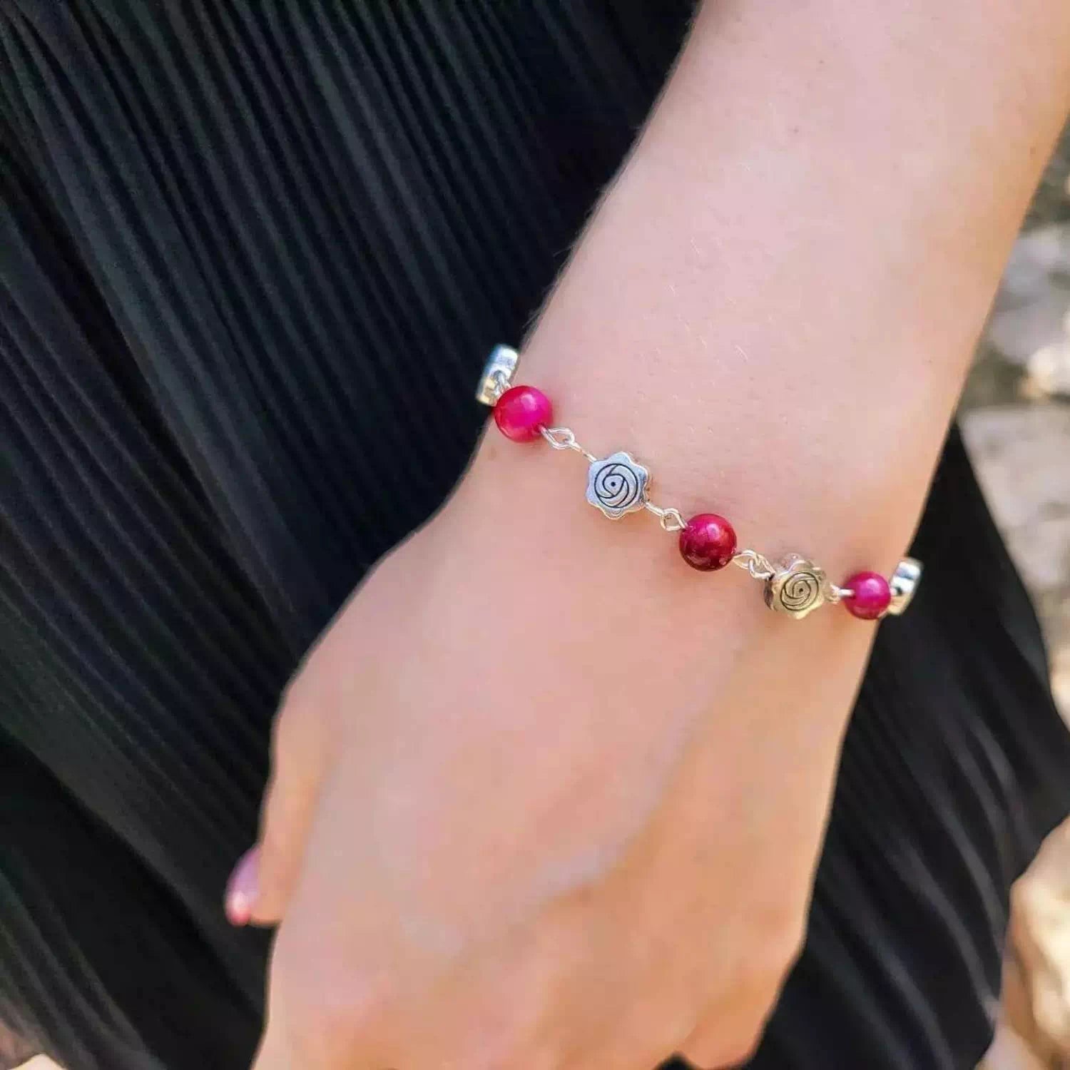 Vue sur le poignet d'une femme portant un bracelet artisanal composé de perles roses fuchsia et de petites roses métalliques argentées.