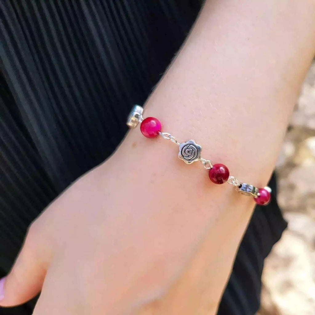 Détail d'un bracelet élégant en œil de tigre rose fuchsia et fleurs argentées, porté par une femme vêtue d'une robe plissée noire.