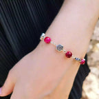 Détail d'un bracelet élégant en œil de tigre rose fuchsia et fleurs argentées, porté par une femme vêtue d'une robe plissée noire.