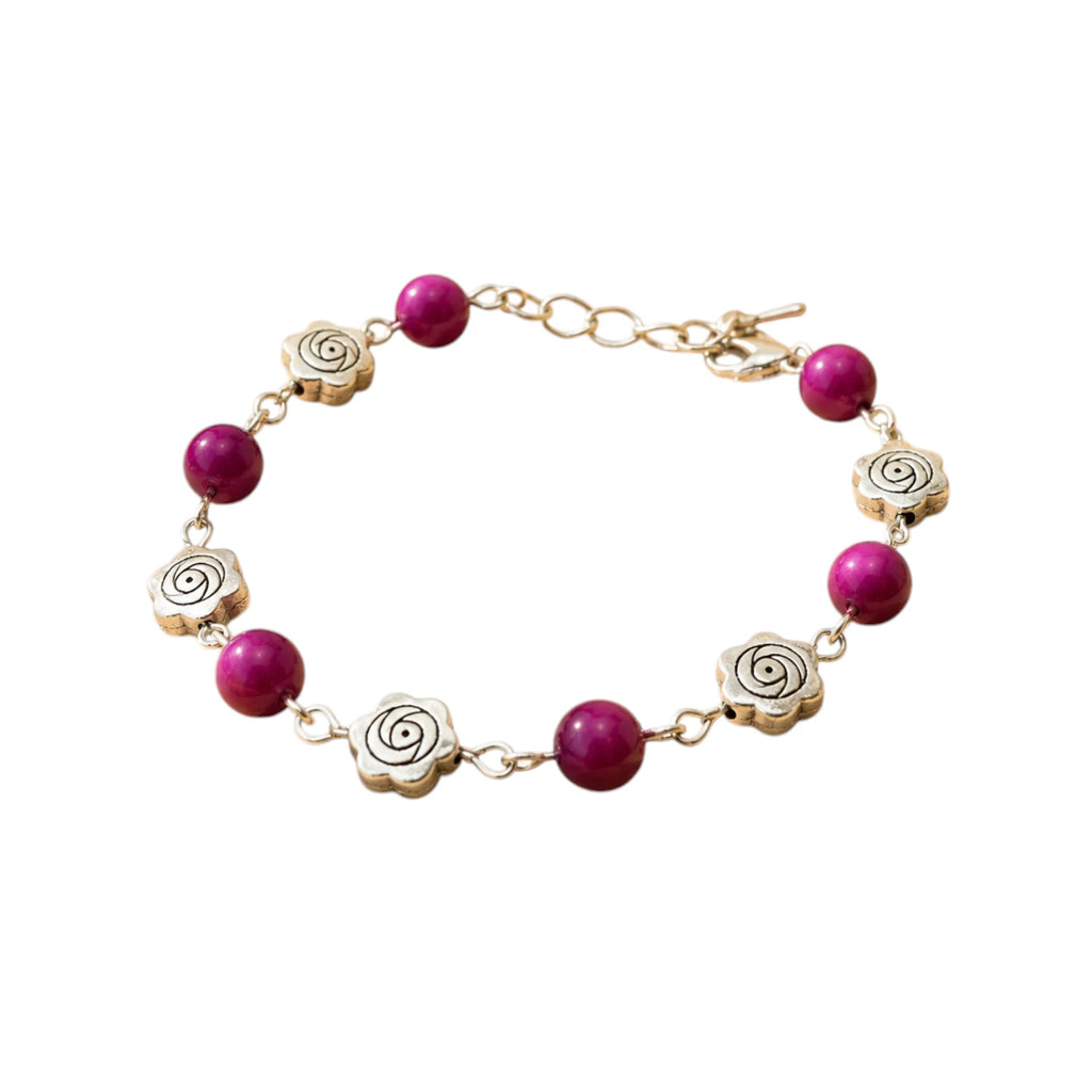 Bracelet fantaisie Jethyka composé de perles rondes en œil de tigre rose fuchsia et de breloques en métal argenté en forme de fleurs de rose, sur fond blanc.