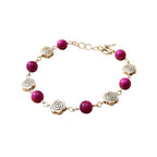 Bracelet fantaisie Jethyka composé de perles rondes en œil de tigre rose fuchsia et de breloques en métal argenté en forme de fleurs de rose, sur fond blanc.