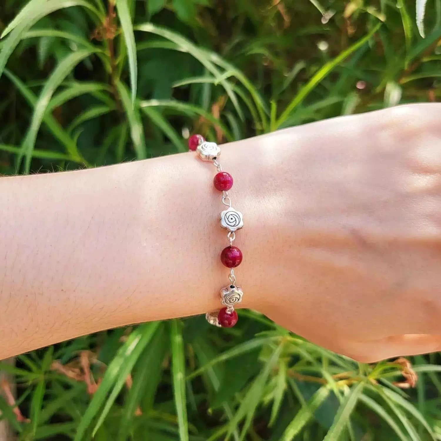 Bracelet fantaisie Jethyka avec perles en pierres naturelles roses et maillons argentés, porté au poignet devant des plantes vertes.