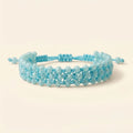Photo de produit sur fond uni beige clair montrant le bracelet bleu ciel de face. Le bijou forme un cercle net, révélant la régularité de son tissage en macramé et l'alignement parfait de ses trois rangées de perles en cristal bleu clair.