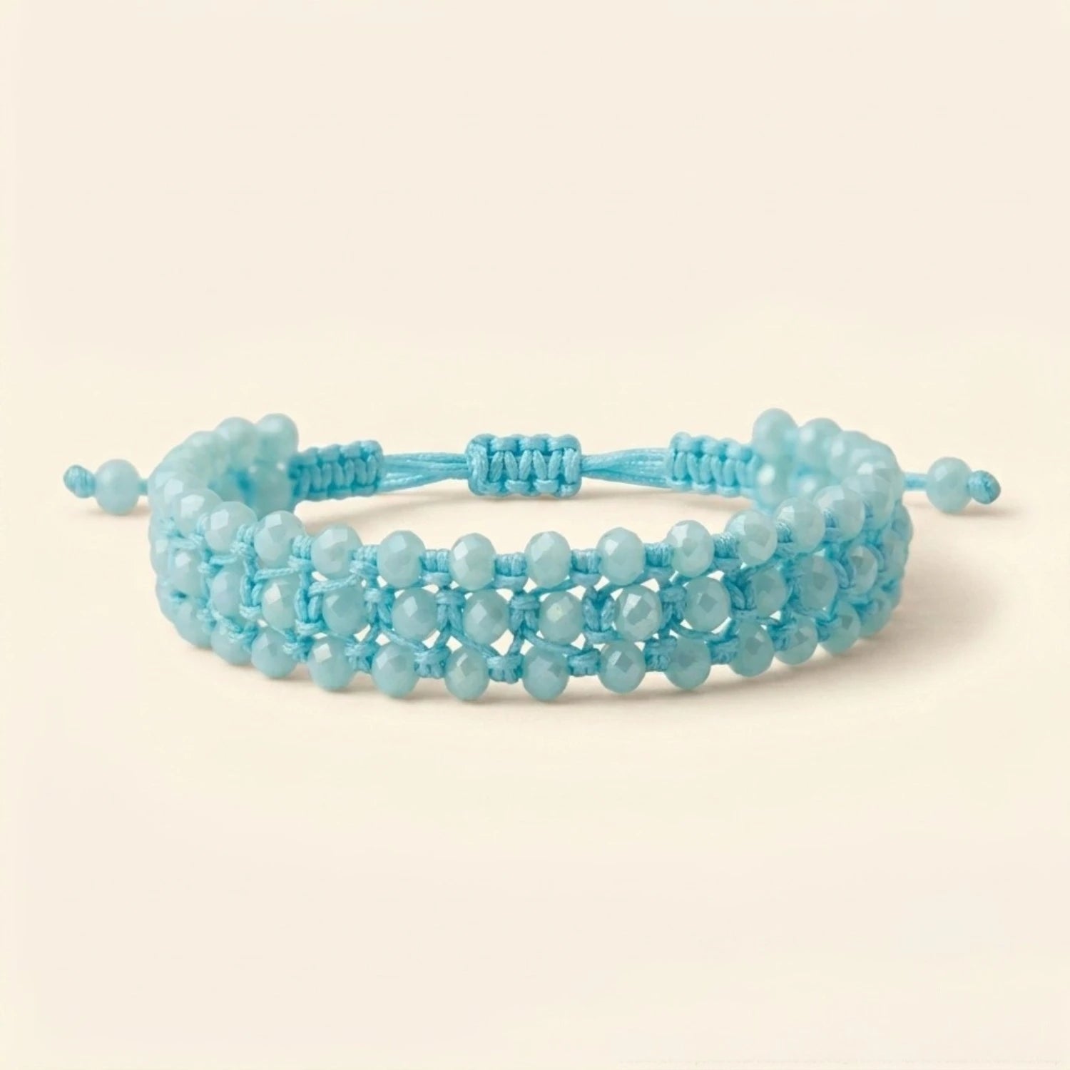 Photo de produit sur fond uni beige clair montrant le bracelet bleu ciel de face. Le bijou forme un cercle net, révélant la régularité de son tissage en macramé et l'alignement parfait de ses trois rangées de perles en cristal bleu clair.