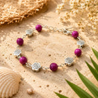 Bijou d'été : bracelet en perles œil de tigre rose et motifs roses argentées posé sur une pierre texturée à côté d'un coquillage et d'un chapeau de paille.