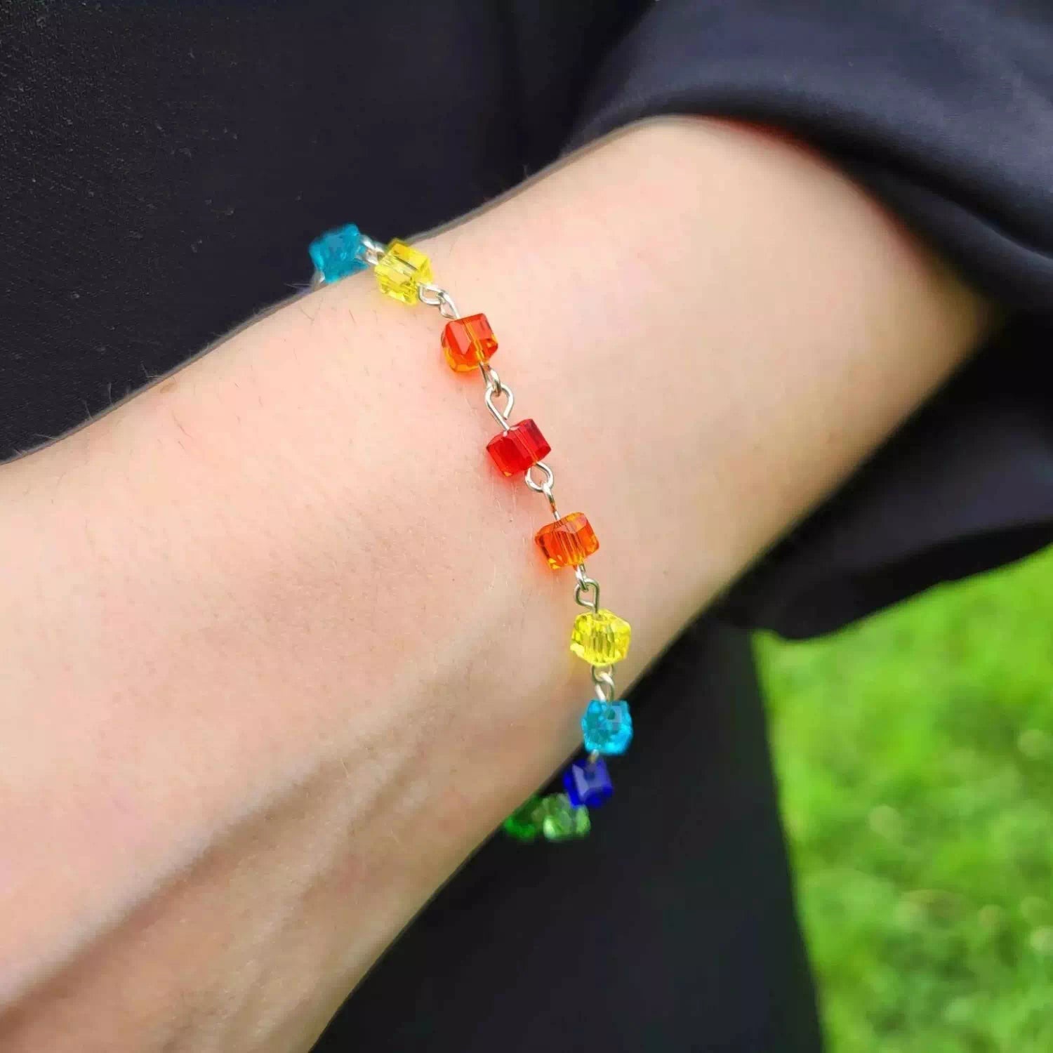 Gros plan d'un bracelet fin pour femme composé de perles cubes en cristal aux couleurs de l'arc-en-ciel.