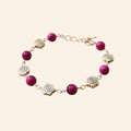 Bracelet de créateur avec perles en pierre naturelle œil de tigre rose et intercalaires roses en métal argenté, présenté sur un fond uni beige clair.