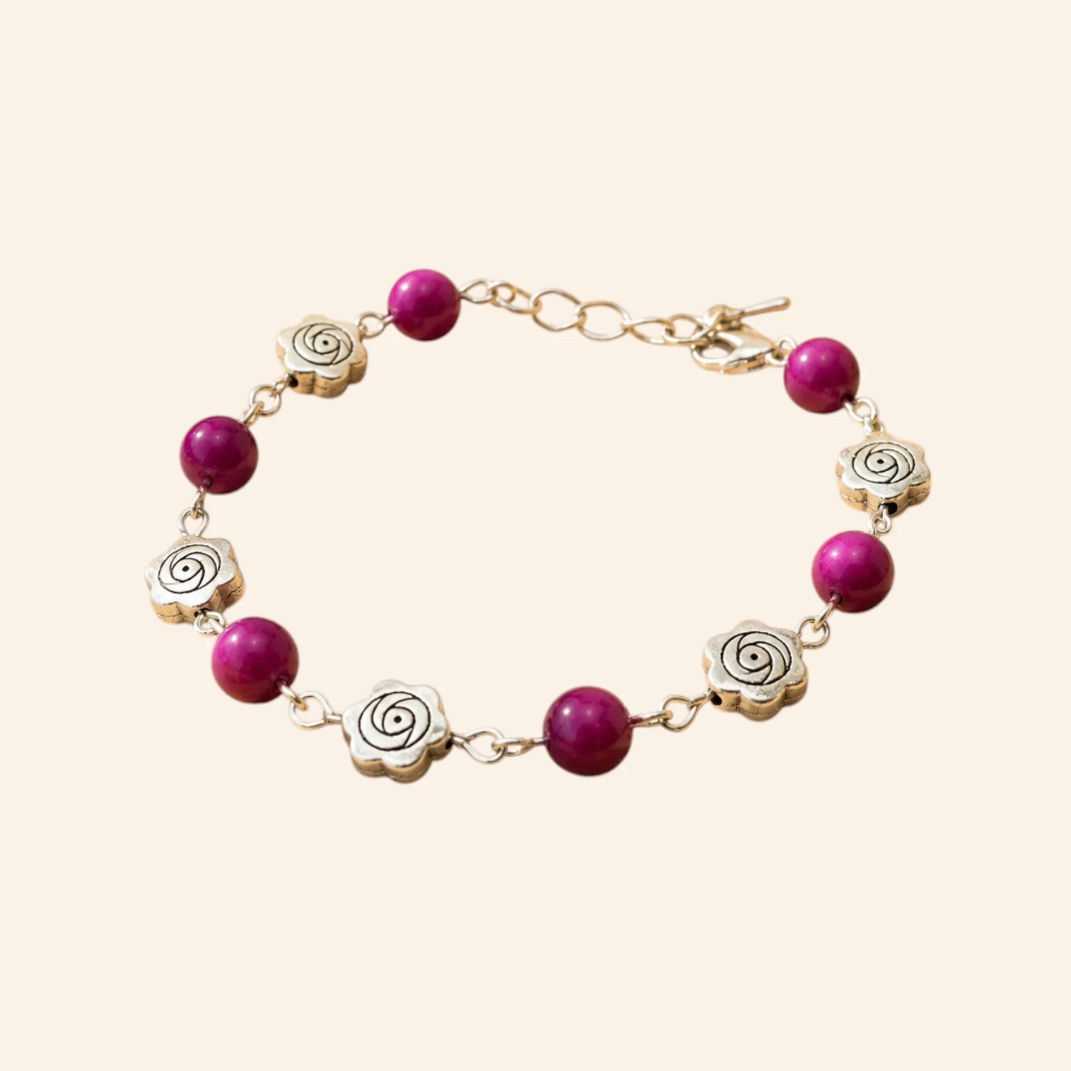 Bracelet de créateur avec perles en pierre naturelle œil de tigre rose et intercalaires roses en métal argenté, présenté sur un fond uni beige clair.