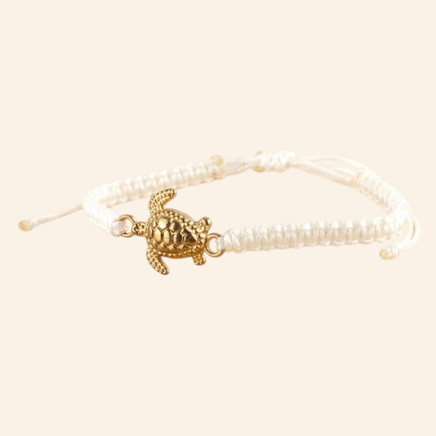 Vue de trois-quarts gauche d'un bracelet cordon blanc ajustable avec une breloque tortue dorée.