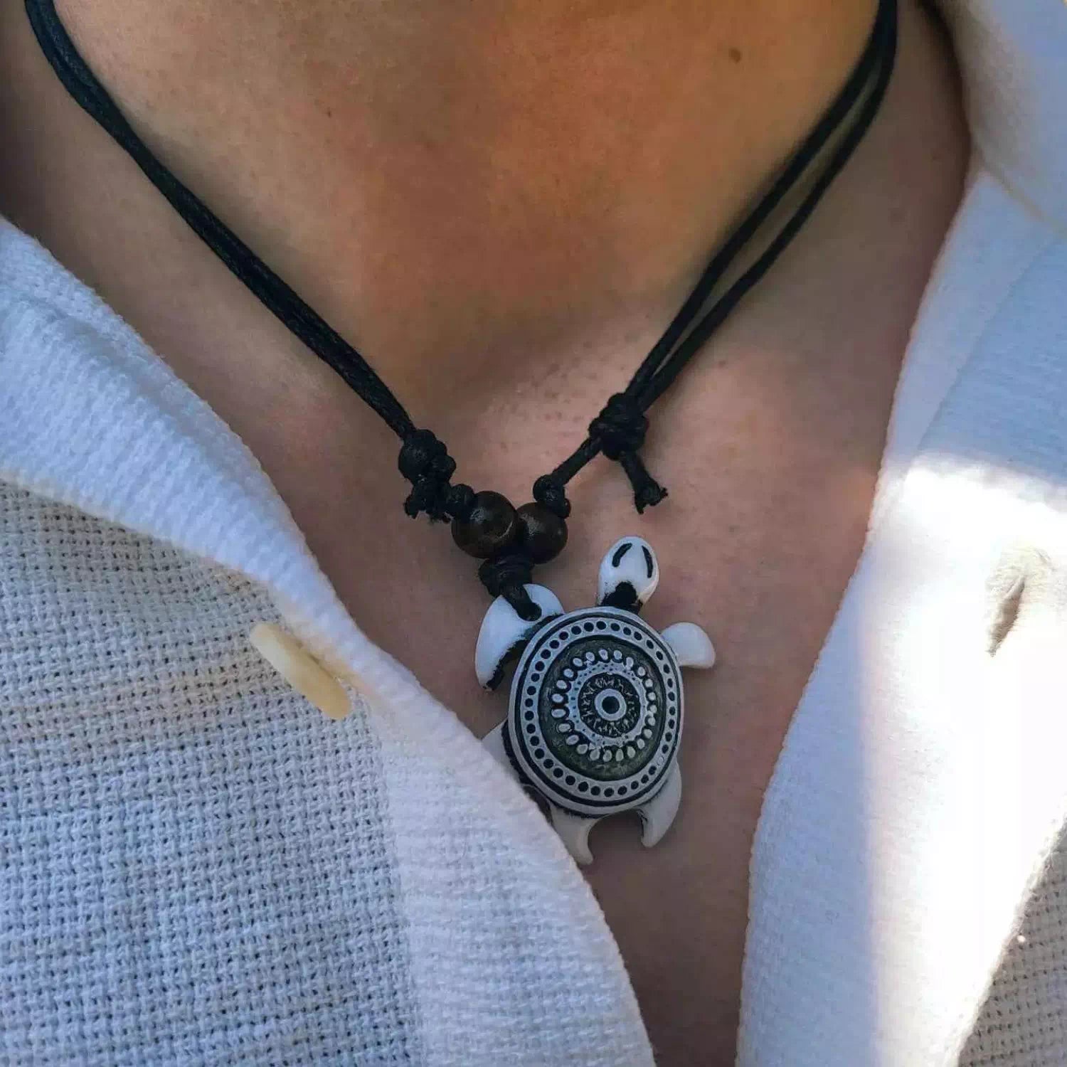 Détail du pendentif tortue blanche à motifs mandala et des perles en bois marron portés au cou.