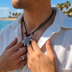 Homme à la plage ajustant son collier pendentif tortue blanche et noire, style bohème et décontracté.
