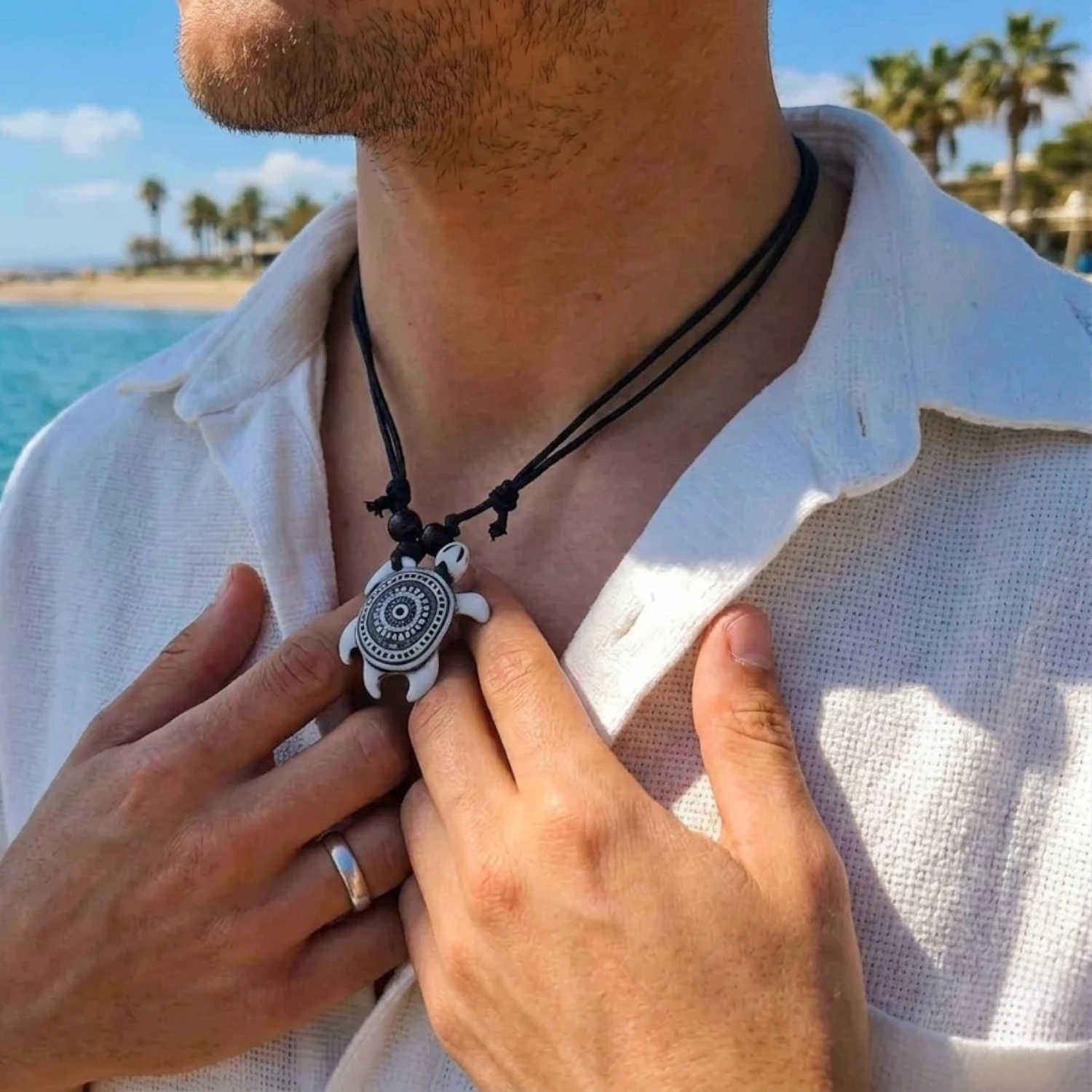 Homme à la plage ajustant son collier pendentif tortue blanche et noire, style bohème et décontracté.