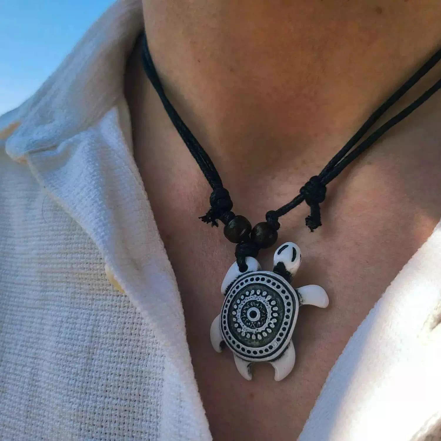 Pendentif tortue de mer blanche et motifs tribaux noirs sur un double cordon ajustable porté par un homme.