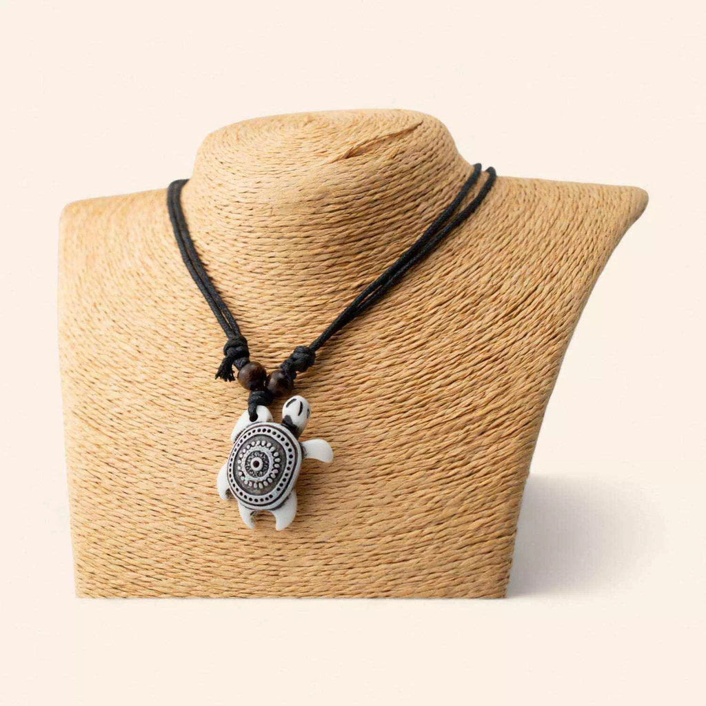 Collier tortue blanche style ethnique avec motifs mandala noirs présenté de face sur un buste de mannequin beige.