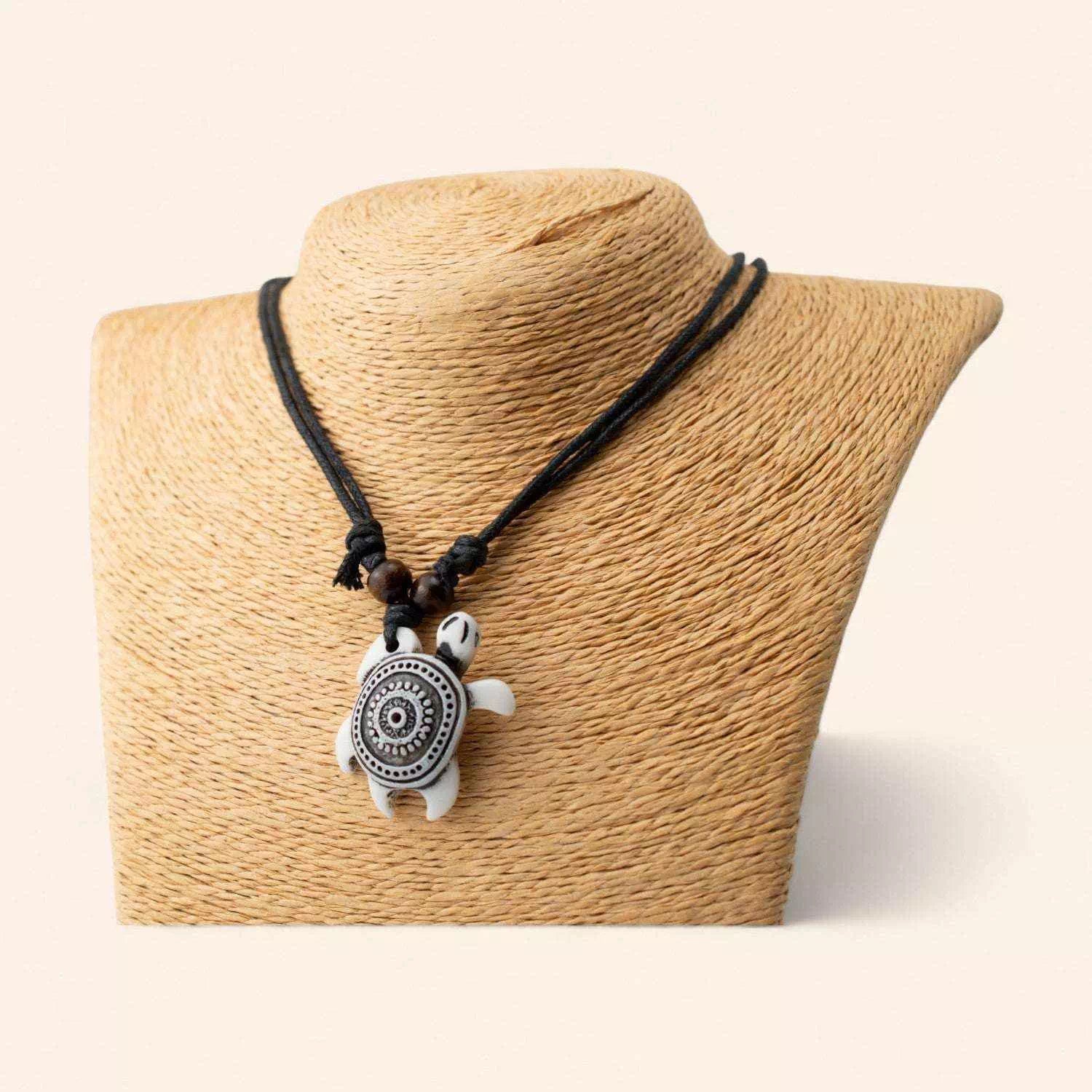 Collier tortue blanche style ethnique avec motifs mandala noirs présenté de face sur un buste de mannequin beige.