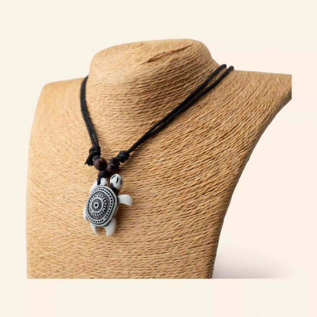 Bijou fantaisie : collier cordon noir avec pendentif tortue marine blanche à motifs géométriques, vue de profil.