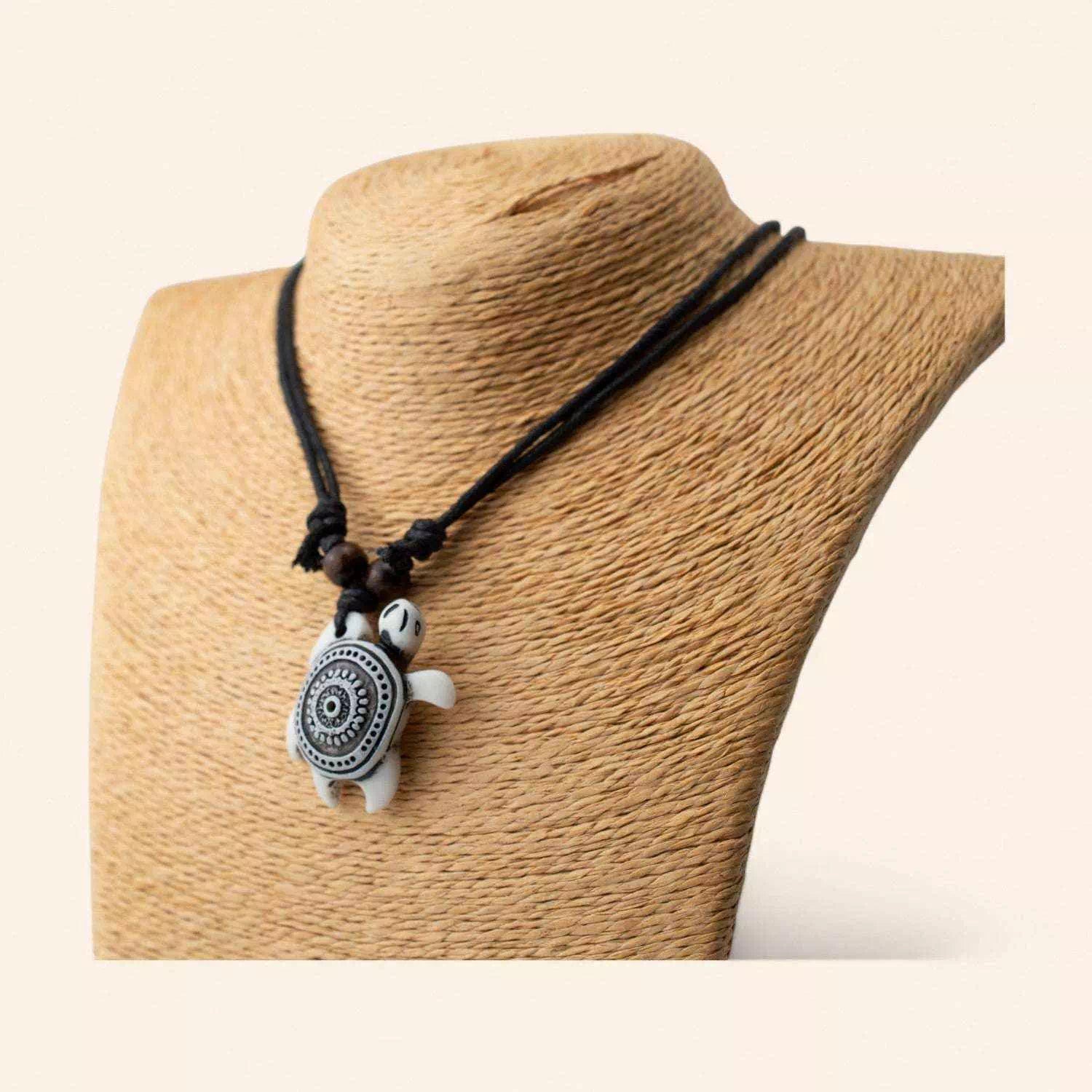 Bijou fantaisie : collier cordon noir avec pendentif tortue marine blanche à motifs géométriques, vue de profil.