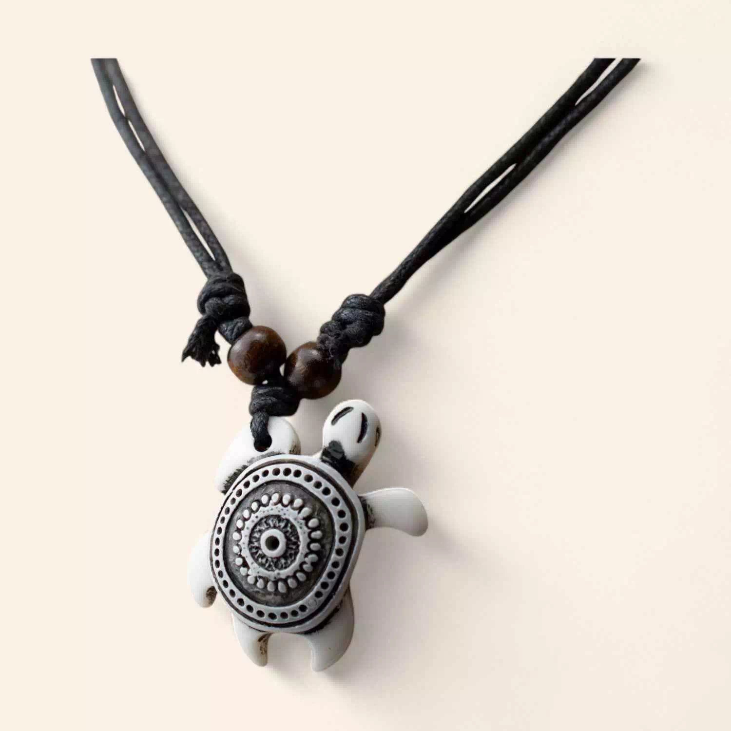 Gros plan sur un pendentif en forme de tortue blanche avec des motifs mandala noirs, monté sur un cordon noir avec perles de bois.
