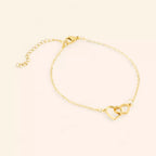 Bracelet JETHYKA en métal doré avec deux cœurs entrelacés, chaîne fine et fermoir mousqueton.