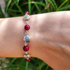 Gros plan d'un bracelet fin pour femme avec perles fuchsia en œil de tigre et roses en métal argenté, porté au poignet sur un fond de verdure.